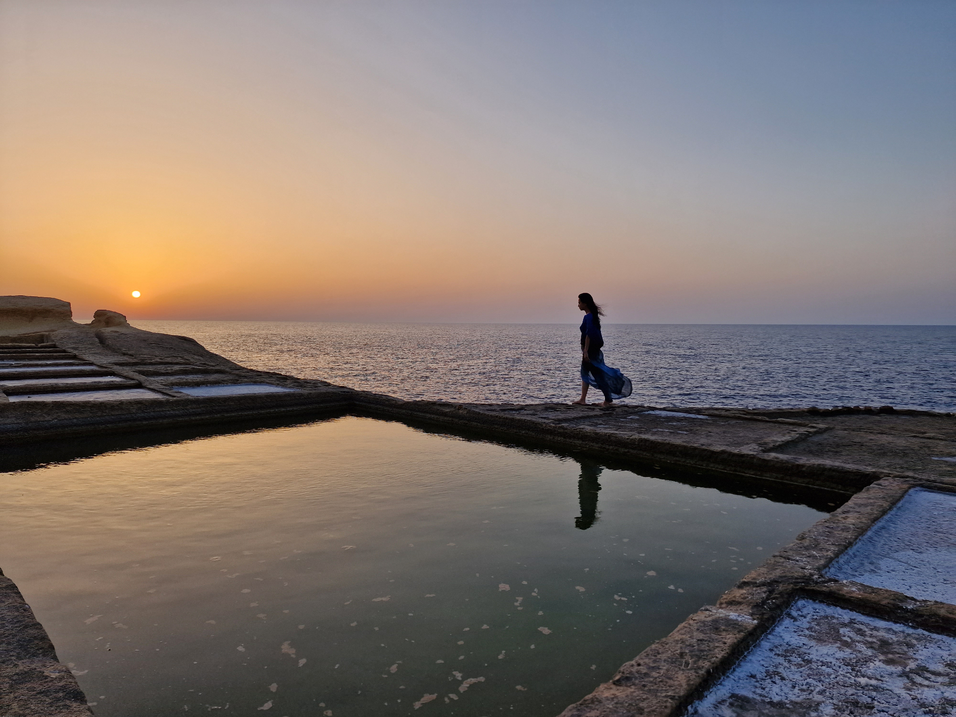 A figure walking the salt pans at sunset on Gozo